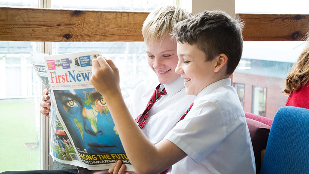 Two boys in school uniform hold and read a copy of First News, smiling